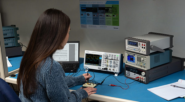 Engineering student using a Tektronix TBS1000C oscilloscope and Keithley bench equipment to learn how to test signals on a DUT